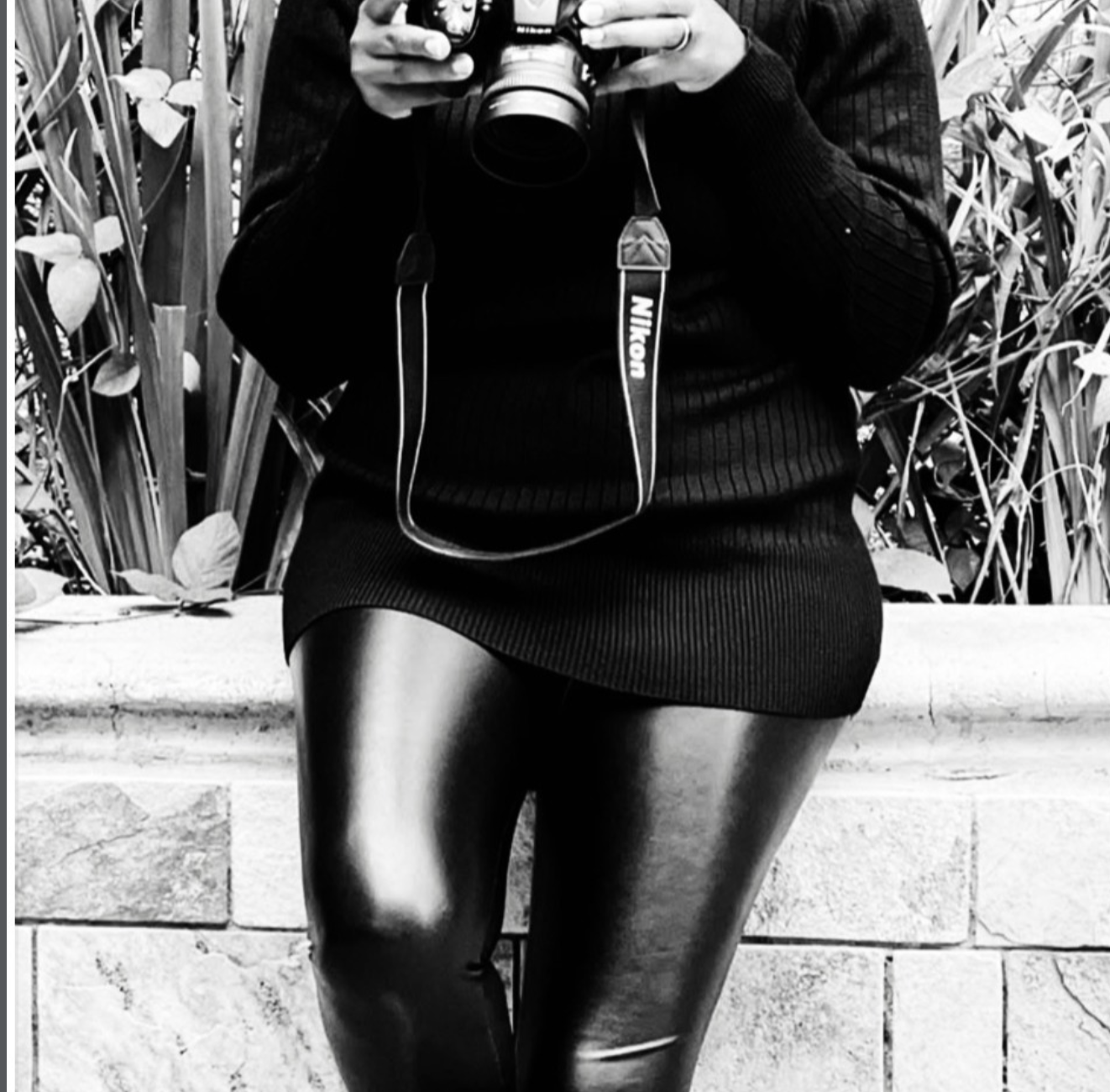A woman in black holding a Nikon camera, framed in soft daylight